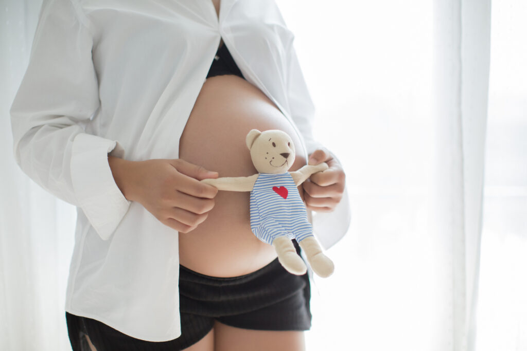 Mujer embarazada coloca oso de peluche sobre su abdomen, como una imagen relacionada con la fertilidad femenina.